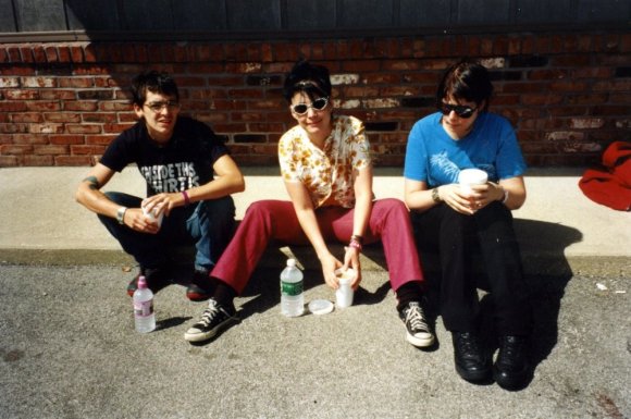 Le Tigre sit on a kerb in front of a brick wall with bottles of water.